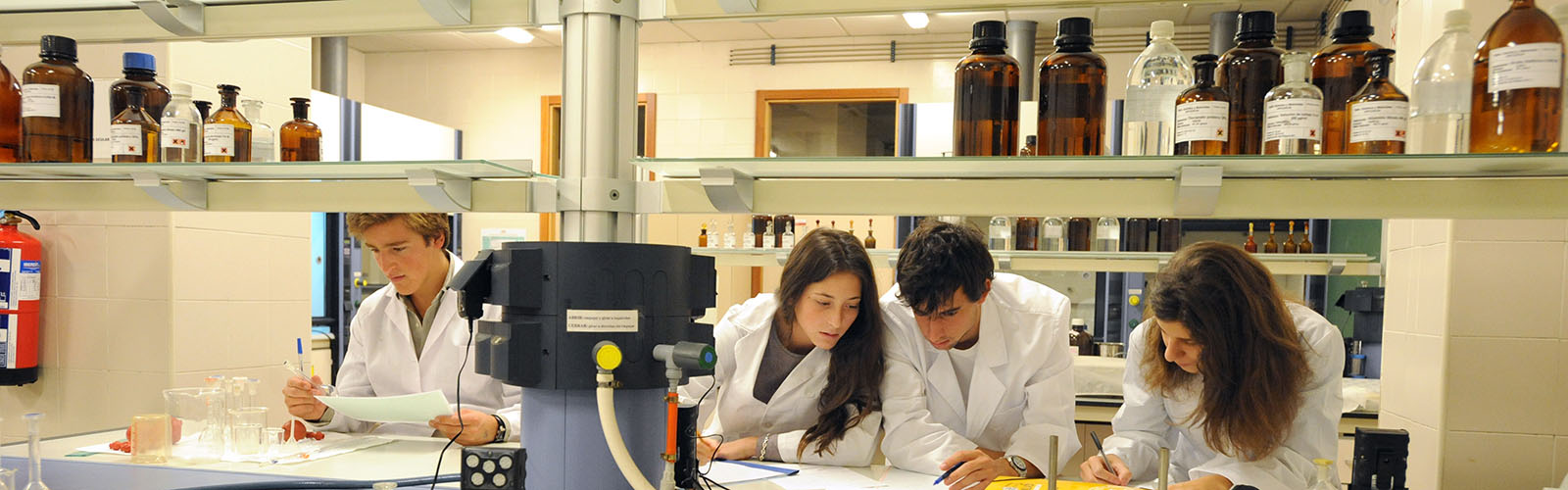 Four students wearing white lab coats while working in a lab.